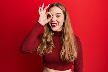 Young blonde woman wearing turtleneck sweater doing ok gesture with hand smiling, eye looking through fingers with happy face.