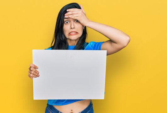 Young hispanic woman holding blank empty banner stressed and frustrated with hand on head, surprised and angry face