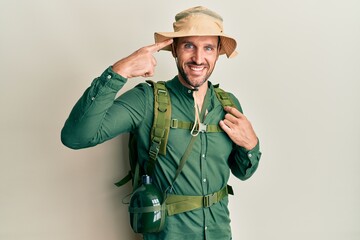 Handsome man with beard wearing explorer hat and backpack smiling pointing to head with one finger, great idea or thought, good memory