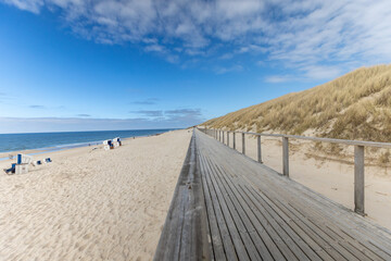 a wooden jetty on a deserted beach in germany. a blue sky with yellow sand and the sea in the background. 