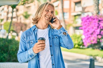 Young blond scandinavian man talking on the smartphone drinking coffee at the city.