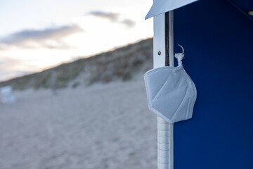 a white ffp2 protective mask hangs in a beach chair on a deserted beach. Vacation 2021 in germany. 