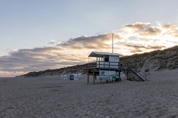 Beautiful beach on the German island of Sylt with white sand and a sunset sky. a lifeguard station and empty  beach chairs.