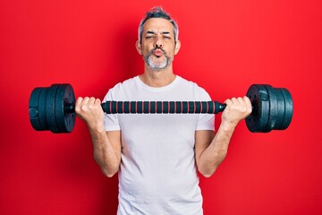 Handsome middle age man with grey hair wearing sportswear using dumbbells looking at the camera blowing a kiss being lovely and sexy. love expression.