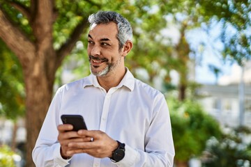 Middle age grey-haired man smiling happy using smartphone at the city.