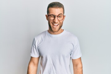 Young caucasian man wearing casual clothes and glasses winking looking at the camera with sexy expression, cheerful and happy face.