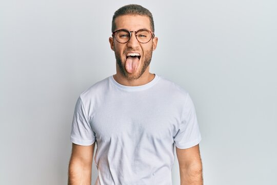 Young caucasian man wearing casual clothes and glasses sticking tongue out happy with funny expression. emotion concept.