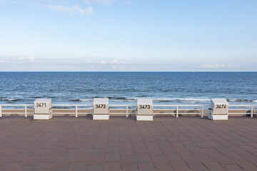 Fototapeta na wymiar an empty promenade leading along a sea. empty beach chairs in front of a blue sky with the north sea in the background. 