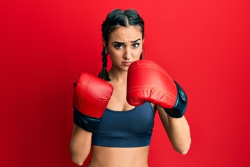 Young brunette girl using boxing gloves skeptic and nervous, frowning upset because of problem....