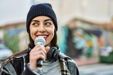 Young hispanic woman smiling happy using headphones and microphone at the city.