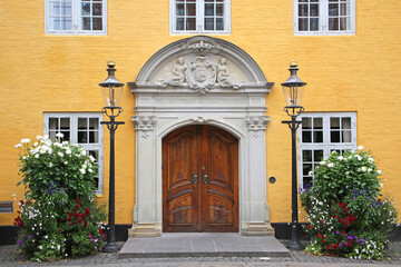 Fototapeta na wymiar Entrance doorway of the Old City Hall. Beautiful historic yellow painted building with a wooden door in the city center, Aalborg, Denmark.