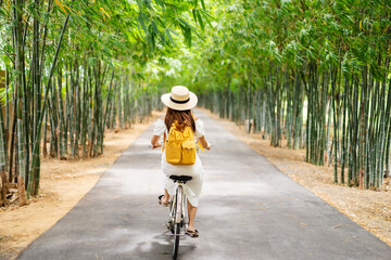 Young happy woman enjoying and riding a bicycle in the bamboo forest while traveling in summer