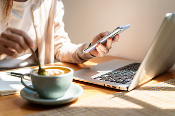 Young woman with cup of coffee using mobile phone and working on laptop at coffee shop