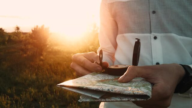 A man with a map and a compass in his hands is looking for a way. Sunset. Close-up. Hiker travels.