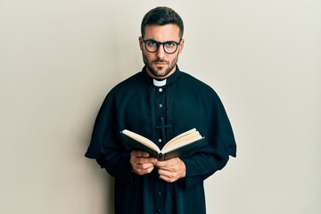 Young hispanic priest man holding bible skeptic and nervous, frowning upset because of problem....