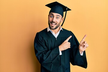 Young hispanic man wearing graduation cap and ceremony robe smiling and looking at the camera...