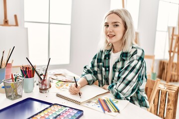 Young artist student girl smiling happy painting sitting on desk at art studio.