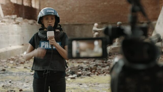 POV Camera view, female war journalist correspondent wearing bulletproof vest and helmet reporting live near destroyed building