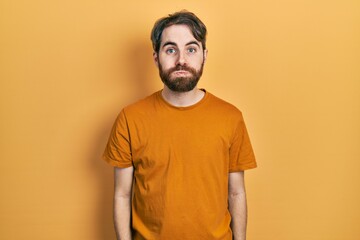 Caucasian man with beard wearing casual yellow t shirt puffing cheeks with funny face. mouth inflated with air, crazy expression.