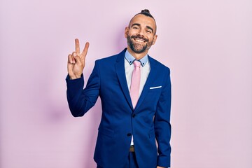 Young hispanic man wearing business suit and tie showing and pointing up with fingers number two while smiling confident and happy.