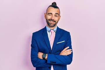 Young hispanic man wearing business suit with arms crossed gesture winking looking at the camera...