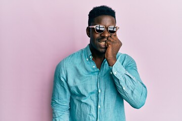Fototapeta premium Handsome business black man wearing stylish sunglasses looking stressed and nervous with hands on mouth biting nails. anxiety problem.