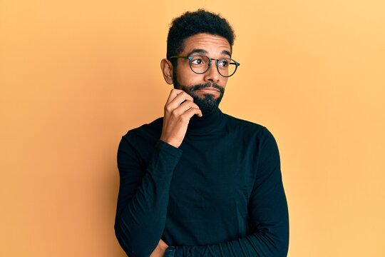 Handsome hispanic man with beard wearing turtleneck sweater thinking concentrated about doubt with finger on chin and looking up wondering