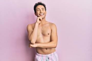 Fototapeta premium Young handsome man wearing swimwear shirtless looking confident at the camera with smile with crossed arms and hand raised on chin. thinking positive.