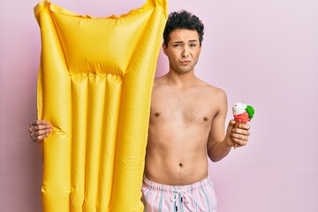 Obraz premium Young handsome man wearing swimsuit holding summer mattress float and icecream depressed and worry for distress, crying angry and afraid. sad expression.
