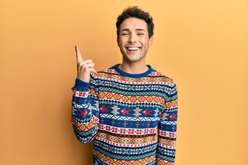 Young handsome man wearing casual winter sweater pointing finger up with successful idea. exited...