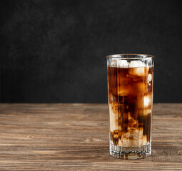 Iced coffee with ice and cream in a tall glass close-up on a black wooden background.