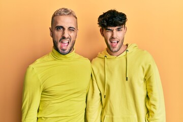 Homosexual gay couple standing together wearing yellow clothes winking looking at the camera with...
