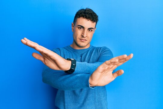 Hispanic young man wearing casual winter sweater rejection expression crossing arms and palms doing negative sign, angry face