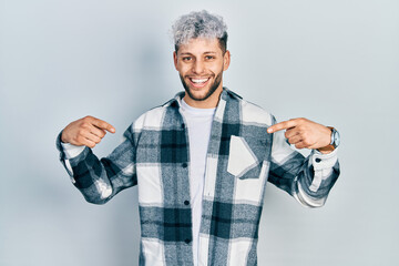 Young hispanic man with modern dyed hair wearing casual shirt looking confident with smile on face,...