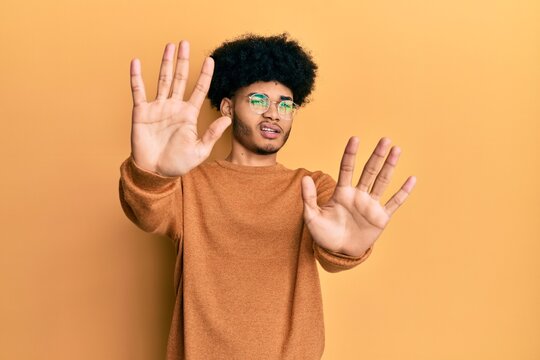 Young african american man with afro hair wearing casual winter sweater afraid and terrified with fear expression stop gesture with hands, shouting in shock. panic concept.