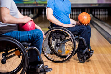 Obraz premium Two young disabled men in wheelchairs playing bowling in the club