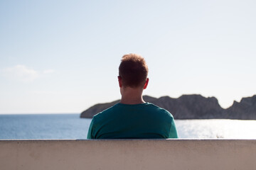 Young man working on a laptop sitting on a bench in a viewpoint in front of the sea. Remote working concept.