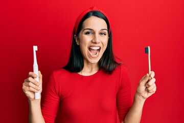 Young hispanic woman choosing electric toothbrush or normal teethbrush celebrating crazy and amazed...