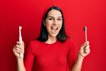 Young hispanic woman choosing electric toothbrush or normal teethbrush celebrating crazy and amazed...