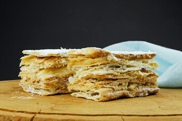 Puff pastry cakes with powdered sugar and cream on wooden board. Close up and space for text. Selective focus.
