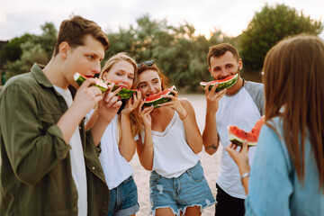 Young friends relaxing on the beach and eating watermelon. Group of people enjoy summer party together. People, lifestyle, travel, nature and vacations concept.