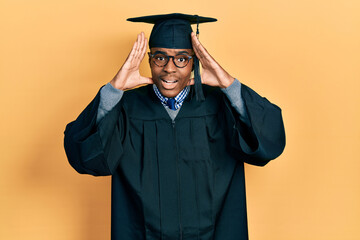 Young african american man wearing graduation cap and ceremony robe smiling cheerful playing peek a boo with hands showing face. surprised and exited