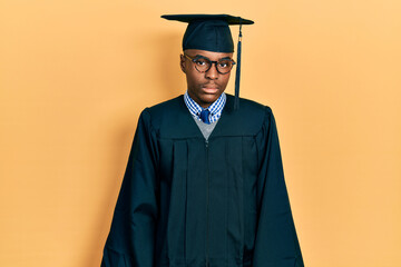 Young african american man wearing graduation cap and ceremony robe relaxed with serious expression...