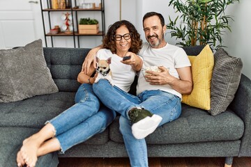 Middle age hispanic couple watching movie and eating popcorn sitting on the sofa at home.