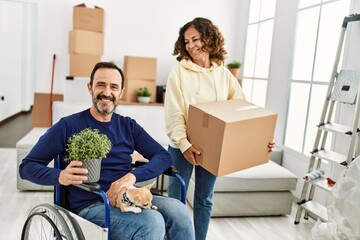 Middle age hispanic couple smiling happy. Man sitting on wheelchair with dog on his legs and woman...