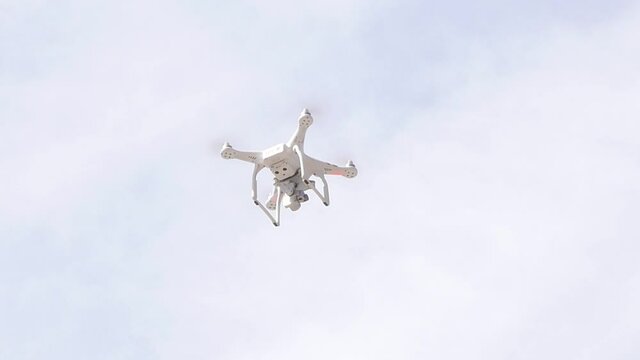 Single modern camera drone hovering, flying, seen from below, object closeup Filming drone up in the air detail shot up close, nobody, drone photography, filmmaking, drone laws concept, sky background