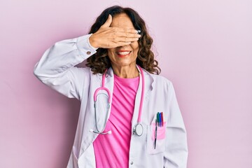 Middle age hispanic woman wearing doctor uniform and glasses smiling and laughing with hand on face covering eyes for surprise. blind concept.