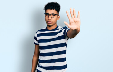 Naklejka premium Young african american man wearing casual clothes and glasses doing stop sing with palm of the hand. warning expression with negative and serious gesture on the face.