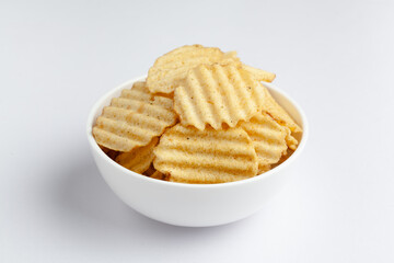 Close up of Wrinkled Wavy Potato Chips in white ceramic bowl, Popular Ready to eat crunchy, salty pale-yellow color over white background