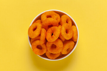 Close up of Popular Ready to eat crunchy and puffed snacks ring tangy orange color in ceramic bowl, salty in white ceramic bowl over yellow background